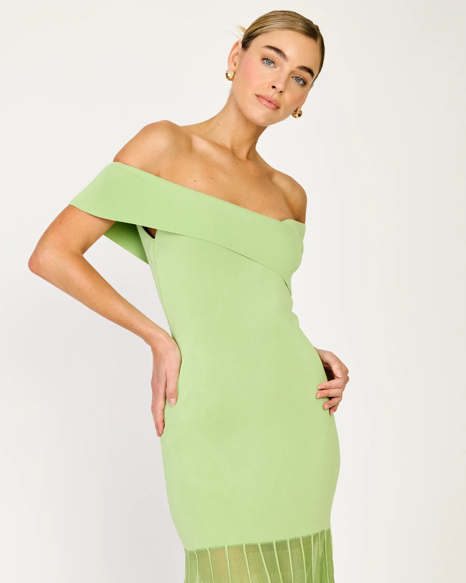 Woman wearing a light green off-shoulder dress against a white background