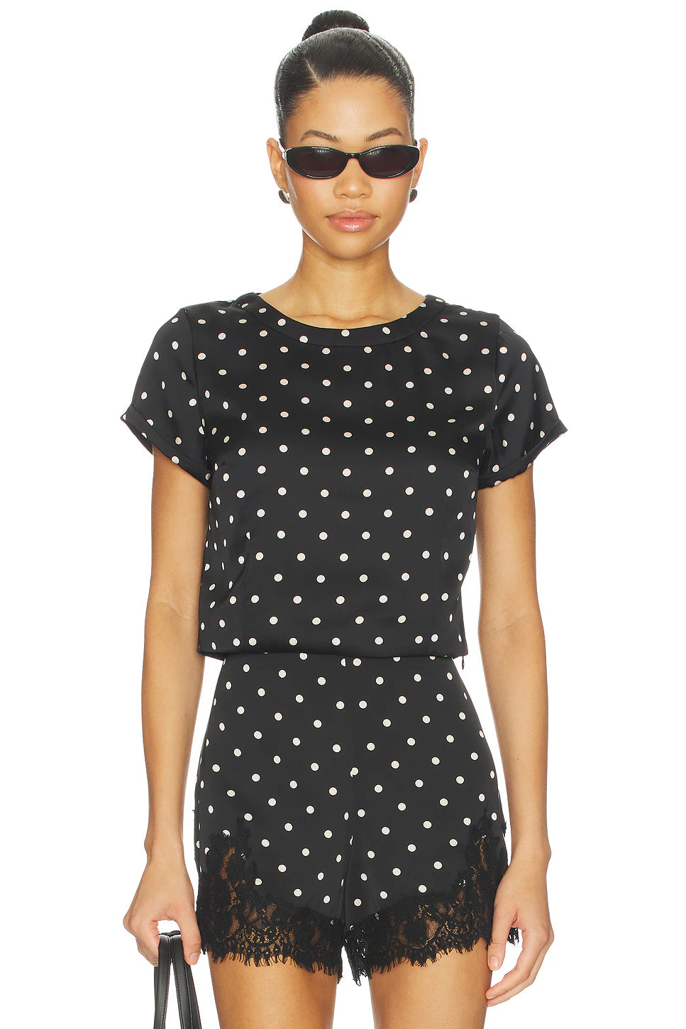Woman wearing a black polka dot outfit with sunglasses on a white background