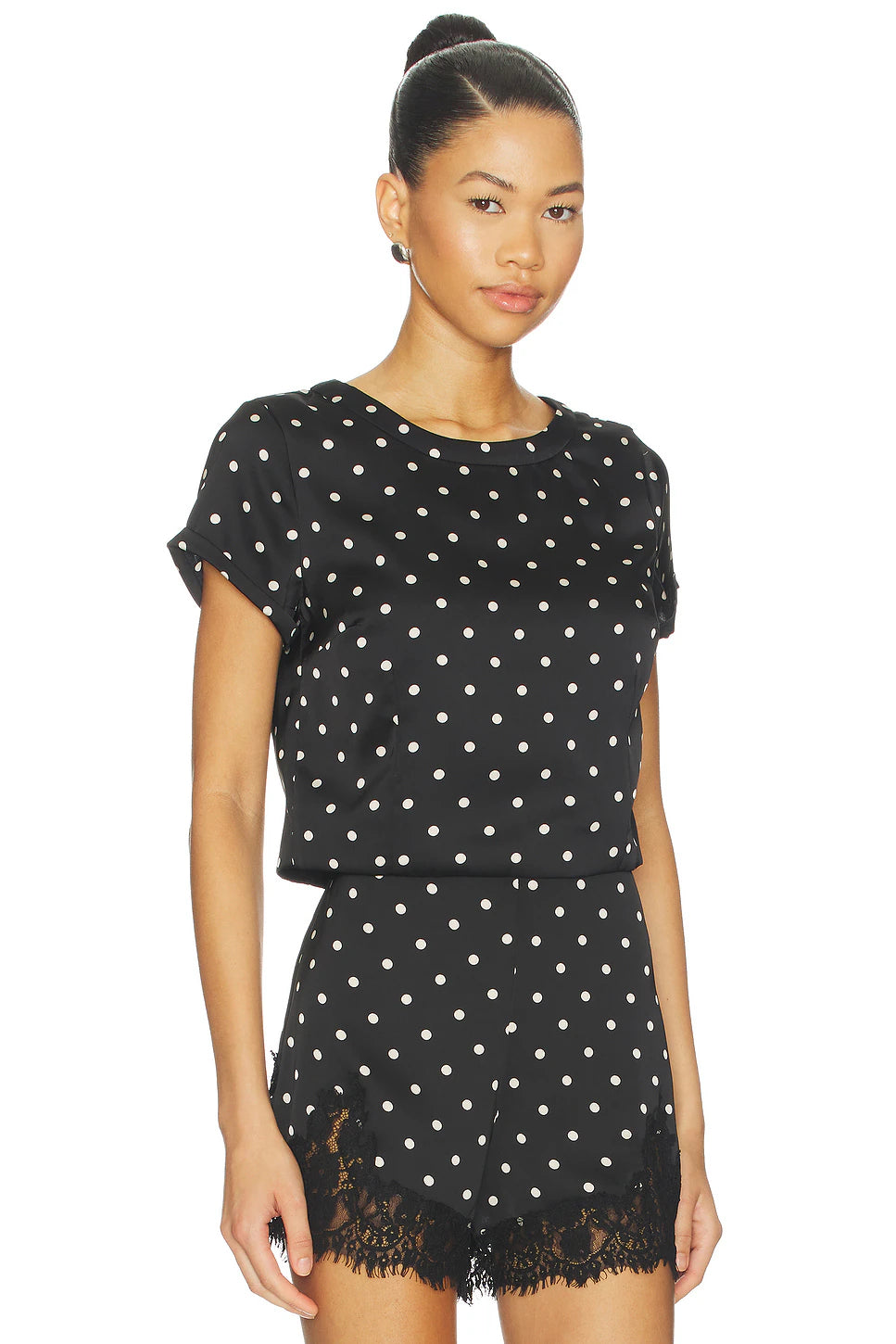 Woman wearing a black polka dot dress with lace hem on a white background