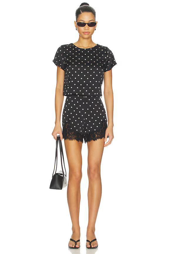 Woman wearing a black polka dot outfit with sunglasses on a white background