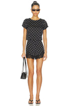 Woman wearing a black polka dot outfit with sunglasses on a white background
