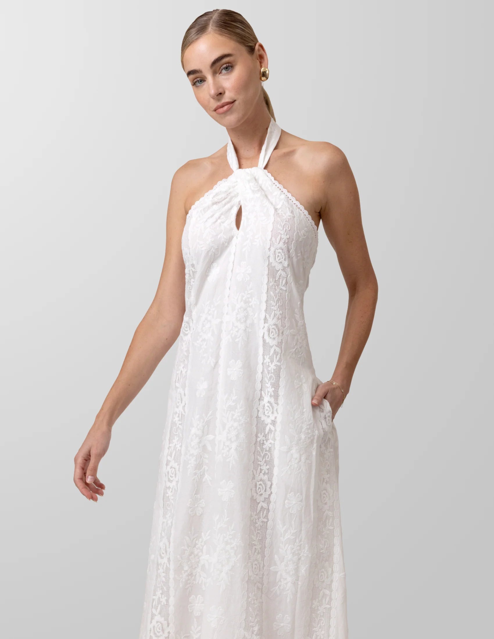 Woman wearing a white halter neck dress against a plain background