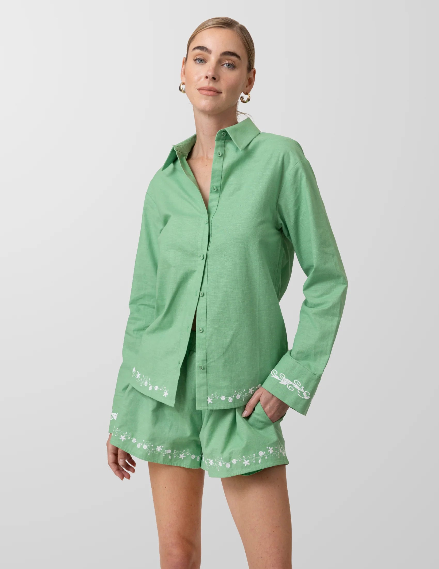Woman wearing a green outfit with white embroidery on a light gray background