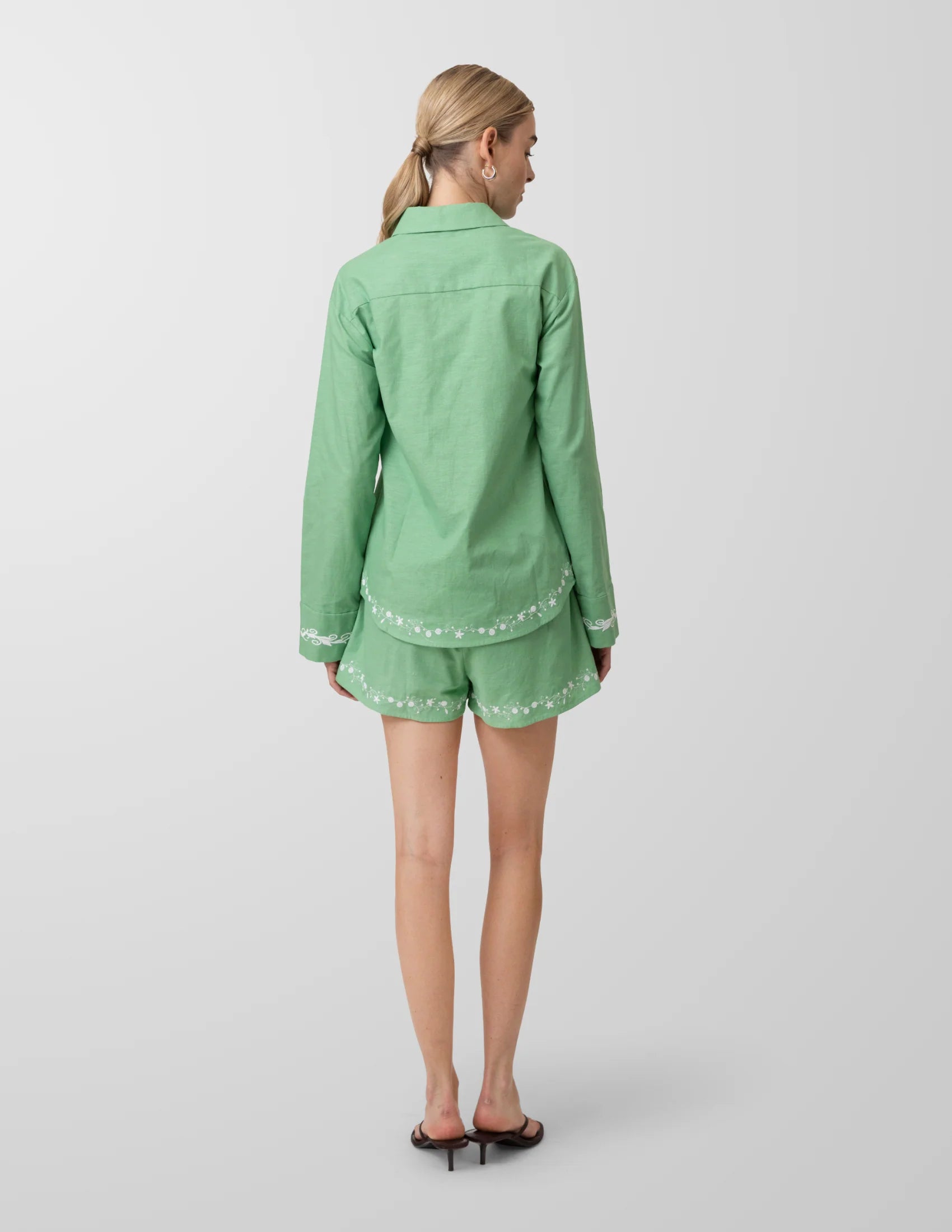 Person wearing a green outfit with white embroidery on a plain background