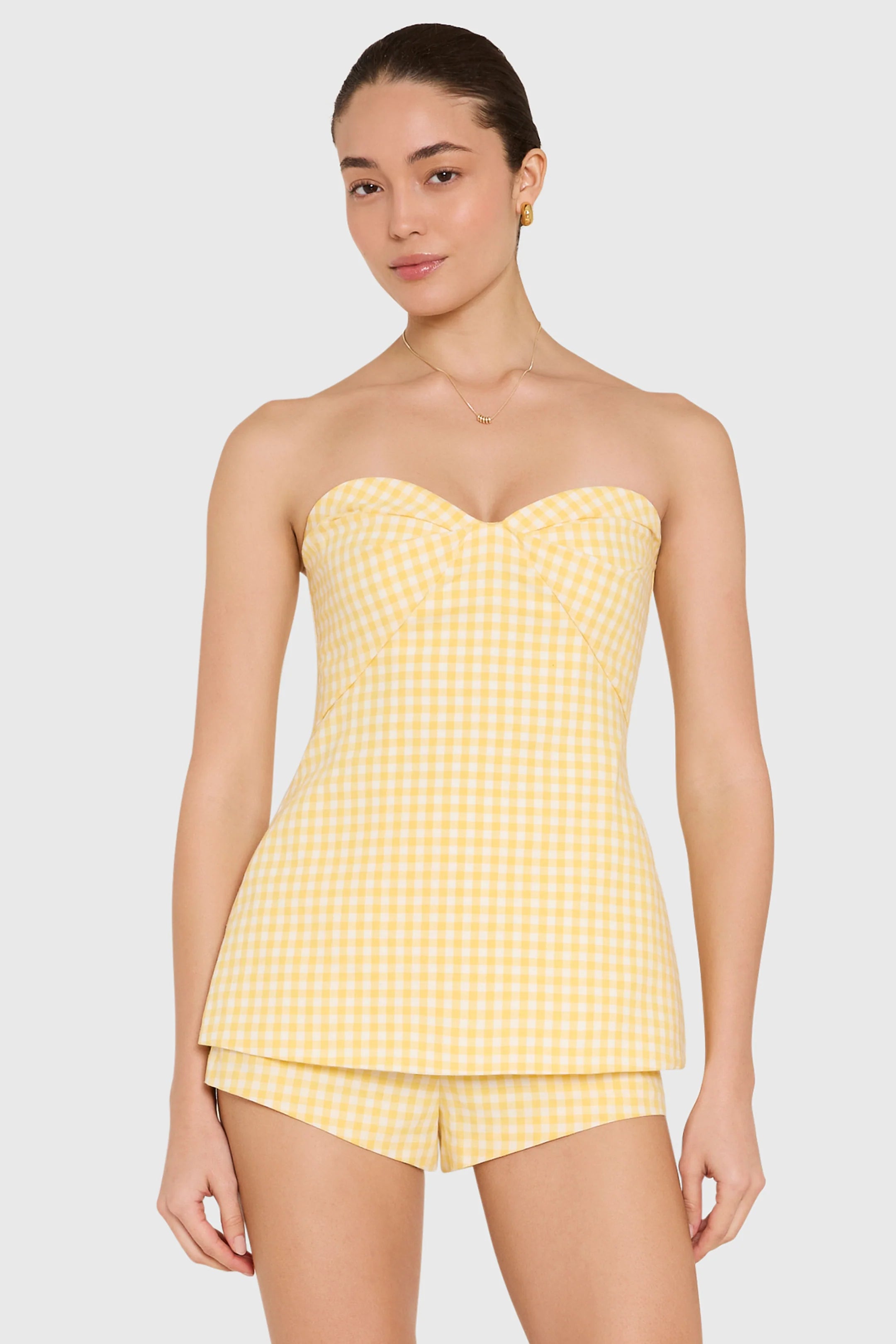 Woman wearing a yellow checkered strapless top and shorts on a white background