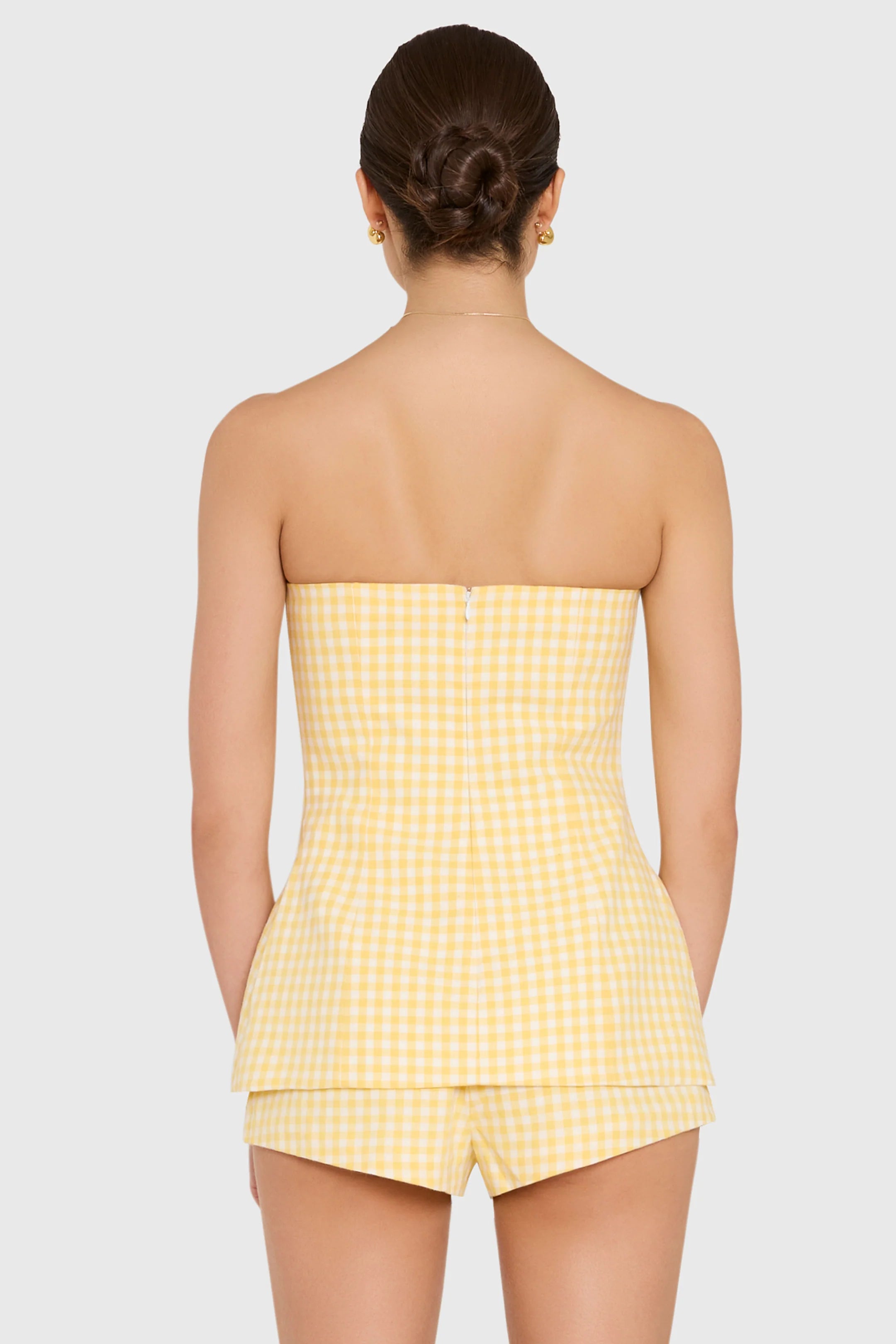 Woman wearing a yellow checkered strapless top and shorts set on a white background