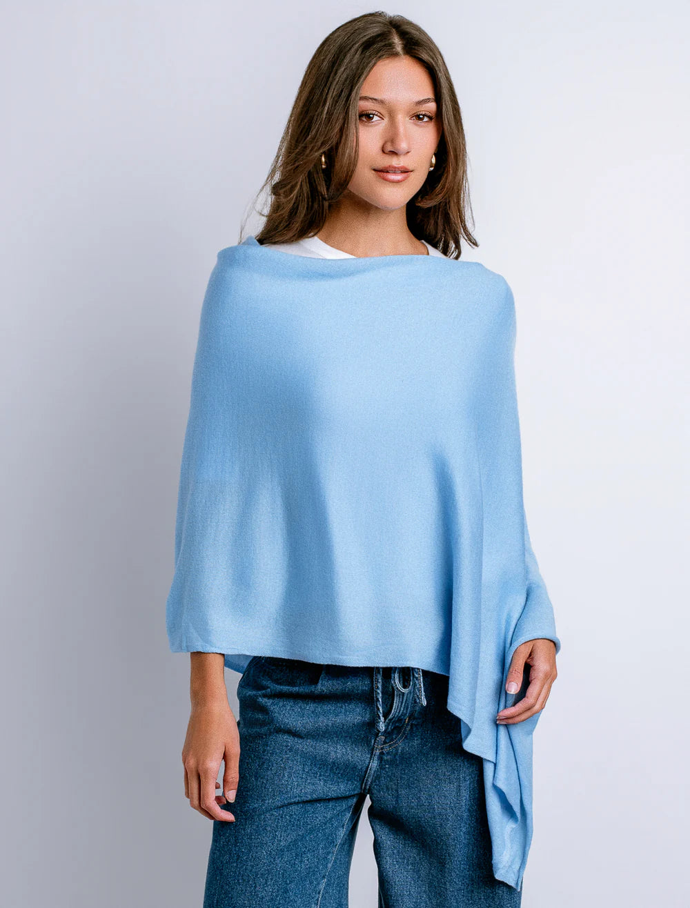 Woman wearing a light blue poncho over a white shirt with jeans on a plain background