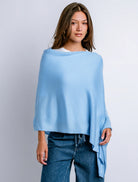 Woman wearing a light blue poncho over a white shirt with jeans on a plain background