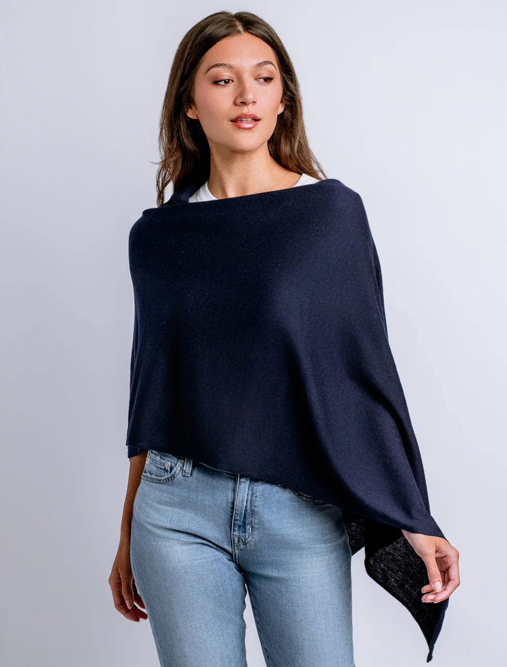 Woman wearing a navy blue poncho over a white shirt and light blue jeans on a gray background