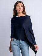 Woman wearing a navy blue poncho over a white shirt and light blue jeans on a gray background