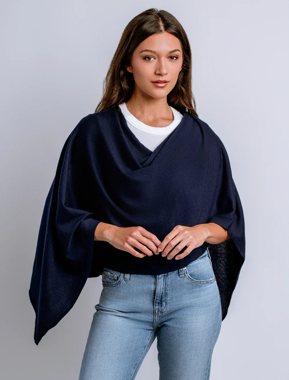 Woman wearing a navy blue poncho over a white shirt and light blue jeans on a gray background