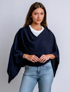 Woman wearing a navy blue poncho over a white shirt and light blue jeans on a gray background