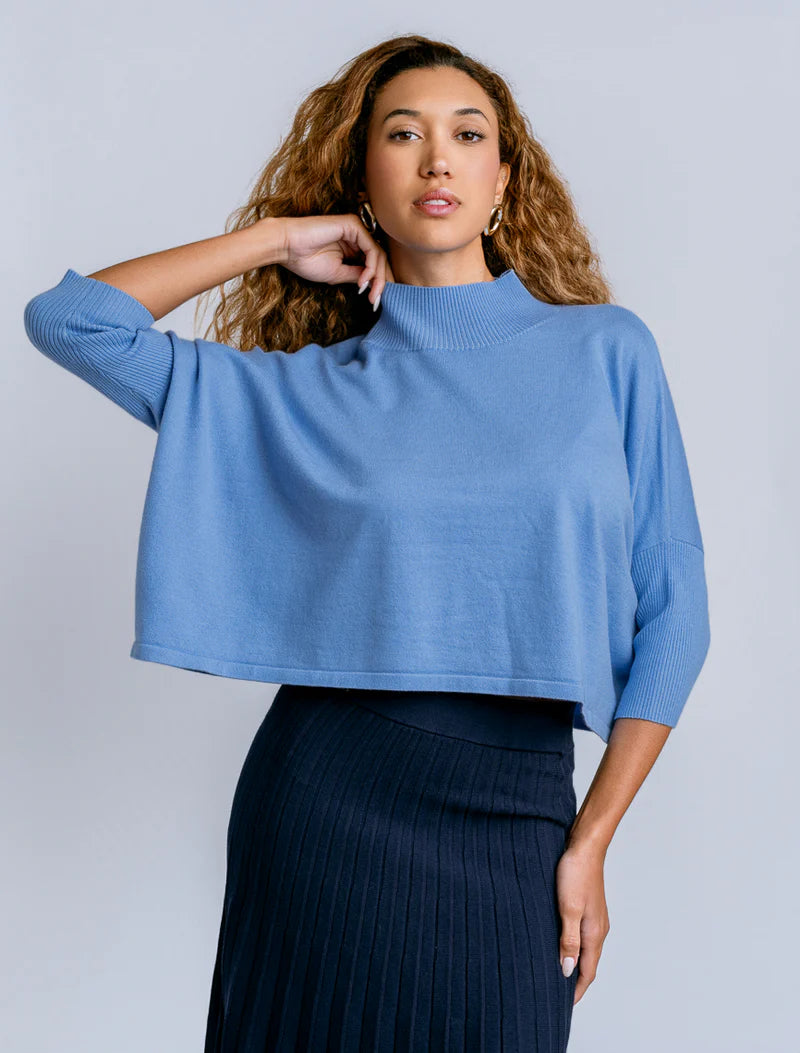 Woman wearing a blue sweater and dark skirt against a light gray background