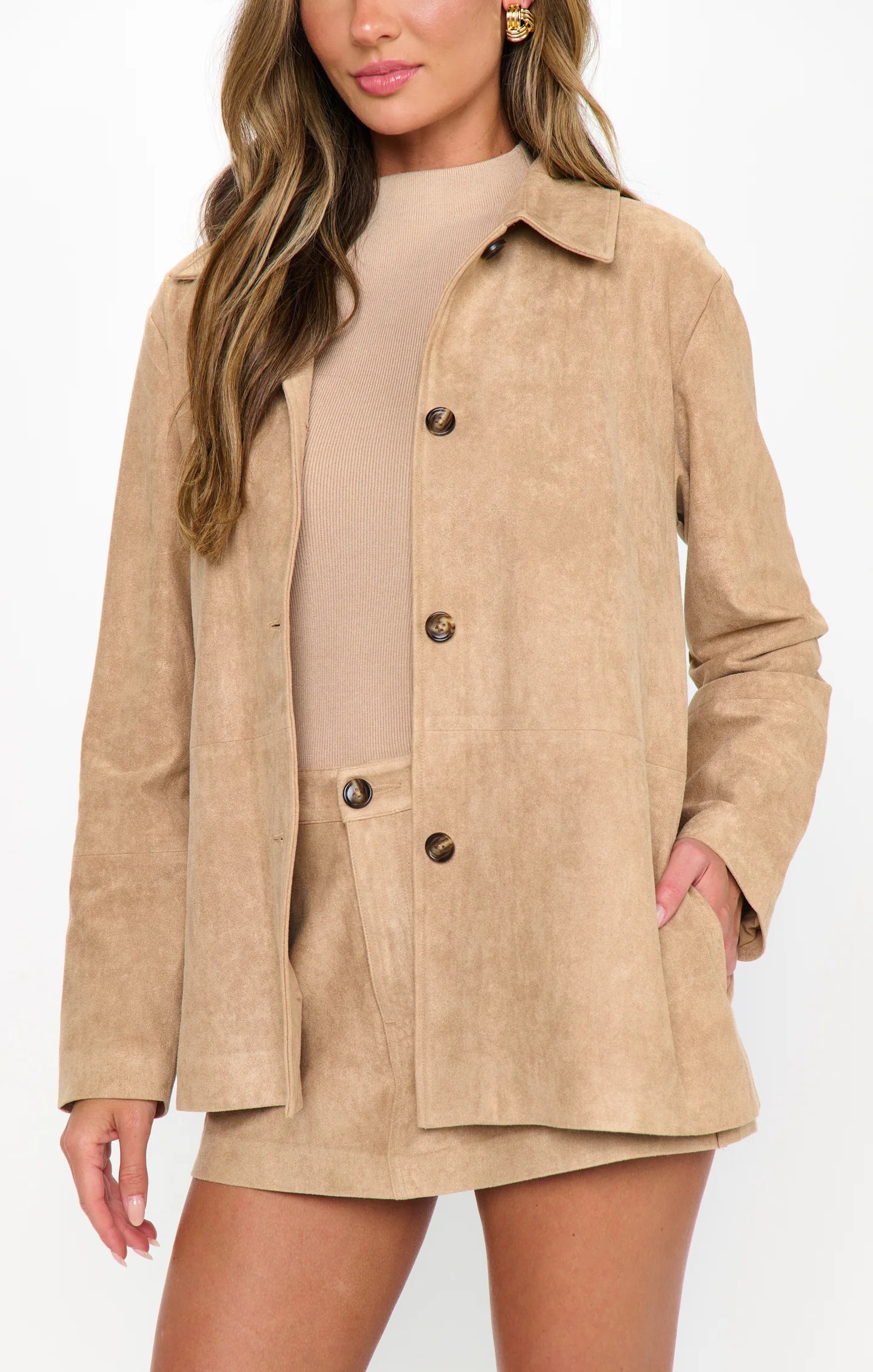 Woman wearing a beige suede jacket over a dress on a white background