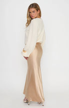 A woman modeling a cream long-sleeve knit top and a floor-length champagne satin skirt against a plain white studio background.