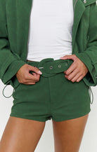 A close-up of a person wearing forest green shorts with a matching belt and drawstring, styled with a white top and a green jacket.