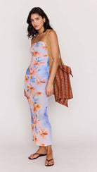 Woman wearing a floral dress holding a brown bag against a white background