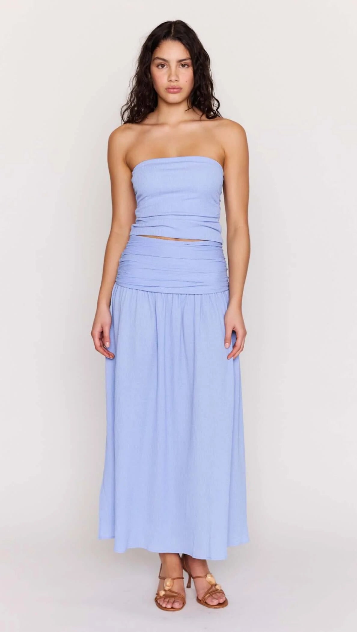 Woman wearing a light blue strapless top and skirt in a bright room.