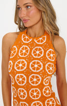 Woman wearing an orange sleeveless top with white patterns on a plain background