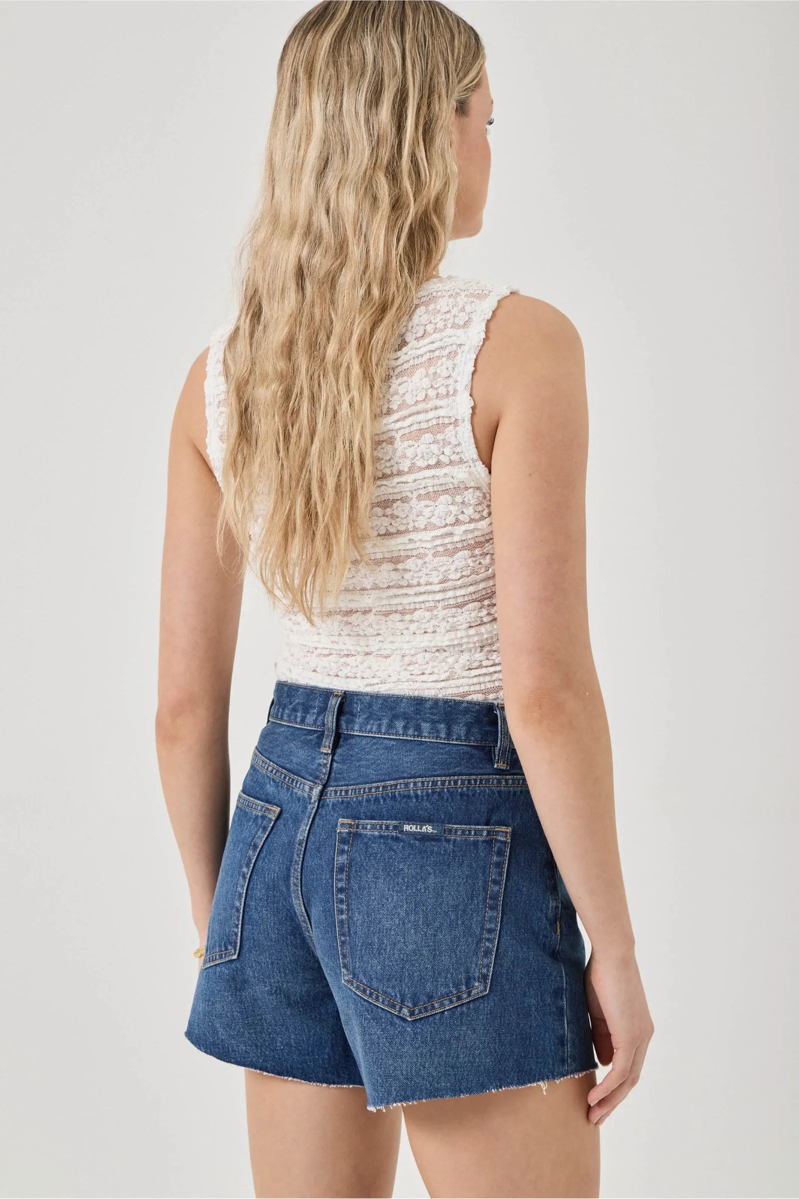 Woman wearing a white sleeveless top and blue denim skirt on a plain background