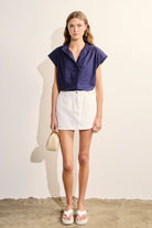 Woman wearing a navy blue top and white shorts against a plain background