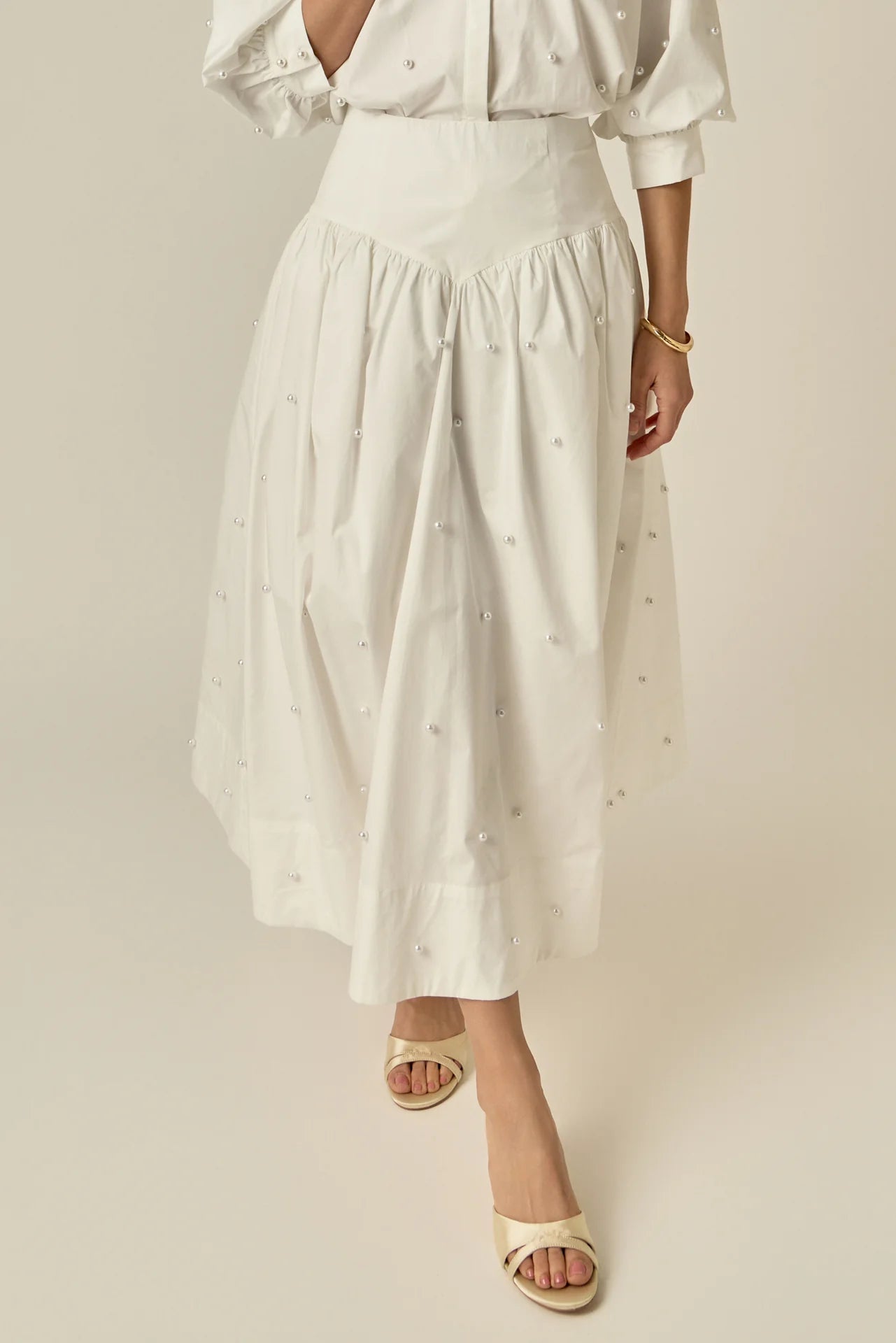 Person wearing a white blouse and skirt with a subtle pattern on a plain background