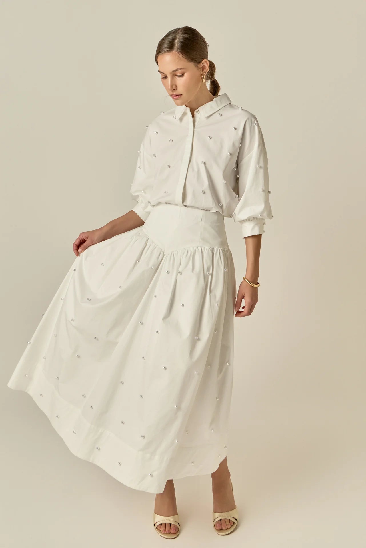 Woman wearing a white outfit with a matching skirt and blouse against a beige background