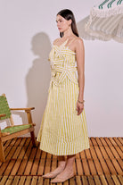 Woman wearing a yellow and white striped dress standing on a wooden floor with a chair and table in the background.