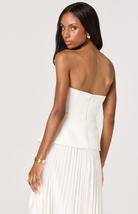 Woman wearing a white strapless dress with a pleated skirt on a plain background