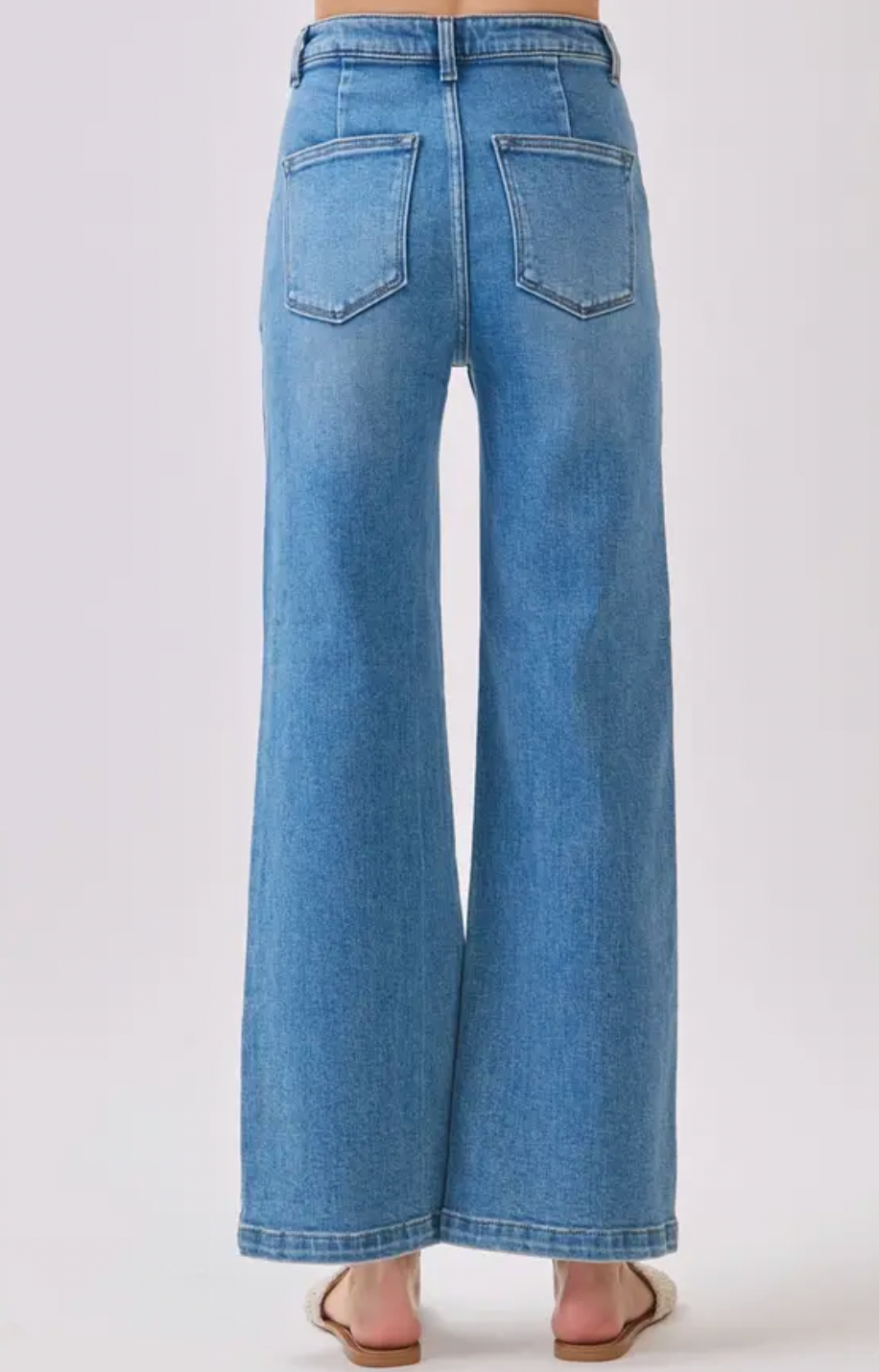 Back view of a person wearing light blue wide-leg denim jeans with back pockets, shown against a plain light gray studio background.