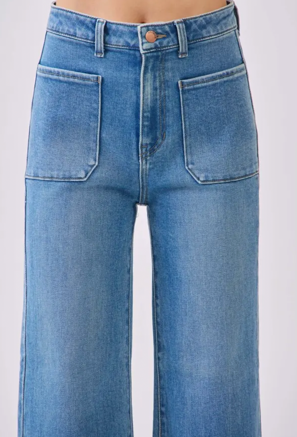 Close-up of a person wearing light blue denim jeans with a high waist, front button closure, belt loops, and large front patch pockets.