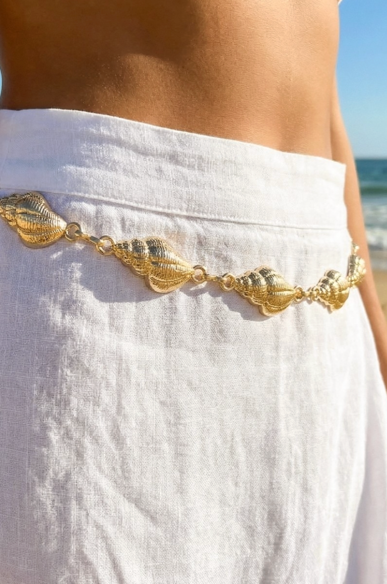 Gold shell belt on a white garment with a beach background