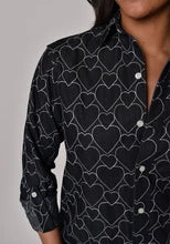 Black shirt with white heart pattern worn by a person against a gray background