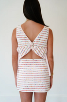 Woman wearing a striped dress with a unique back design on a plain background
