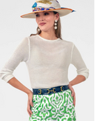 Woman wearing a white sweater, colorful hat, and green patterned skirt on a light gray background