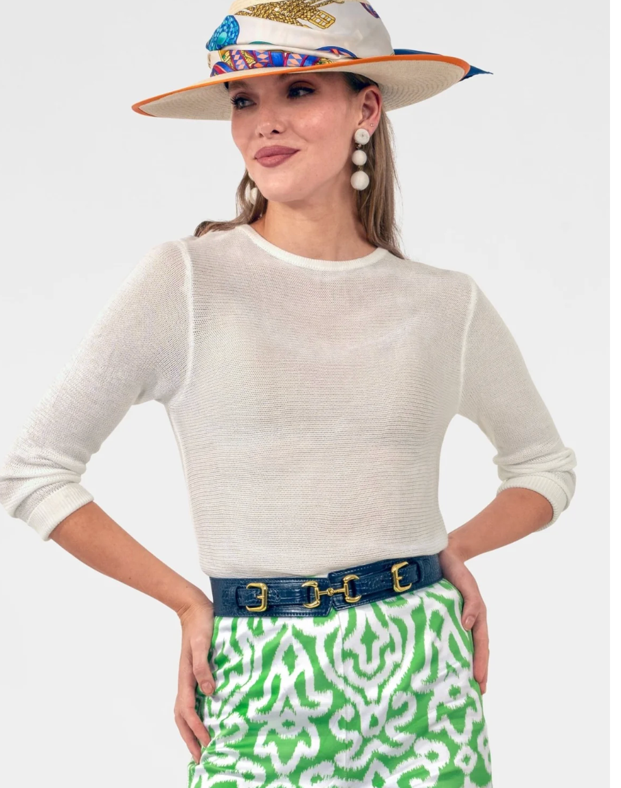 Woman wearing a white sweater, colorful hat, and green patterned skirt on a light gray background