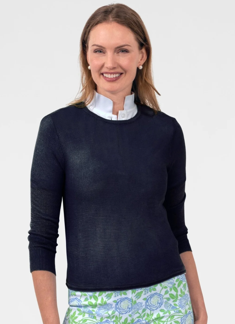 Woman wearing a navy sweater over a white shirt with a floral skirt on a plain background