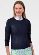 Woman wearing a navy sweater over a white shirt with a floral skirt on a plain background