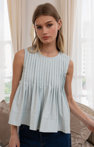 Woman wearing a light blue pleated top in a softly lit room.