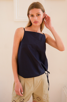 Woman wearing a navy sleeveless top and beige pants against a plain background