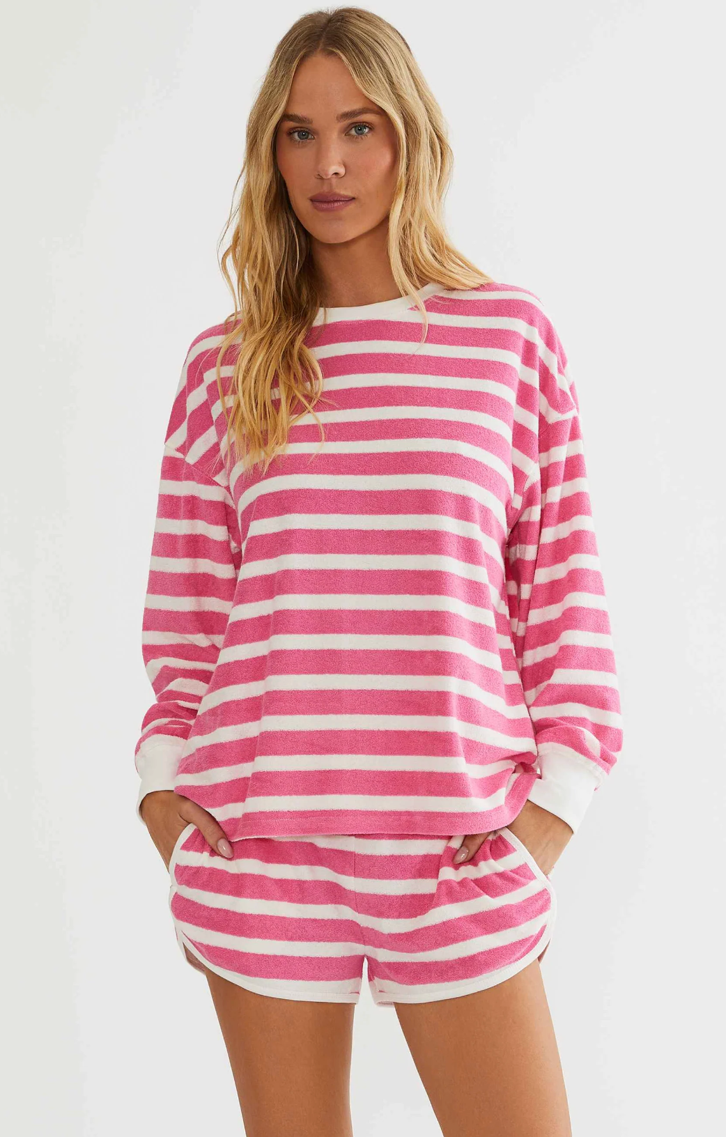 A woman modeling a pink and white horizontally striped long-sleeve top and matching shorts against a plain light background.