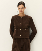 A model wearing a dark brown cropped corduroy jacket with gold-tone buttons and matching dark brown corduroy trousers, photographed against a plain off-white studio background.