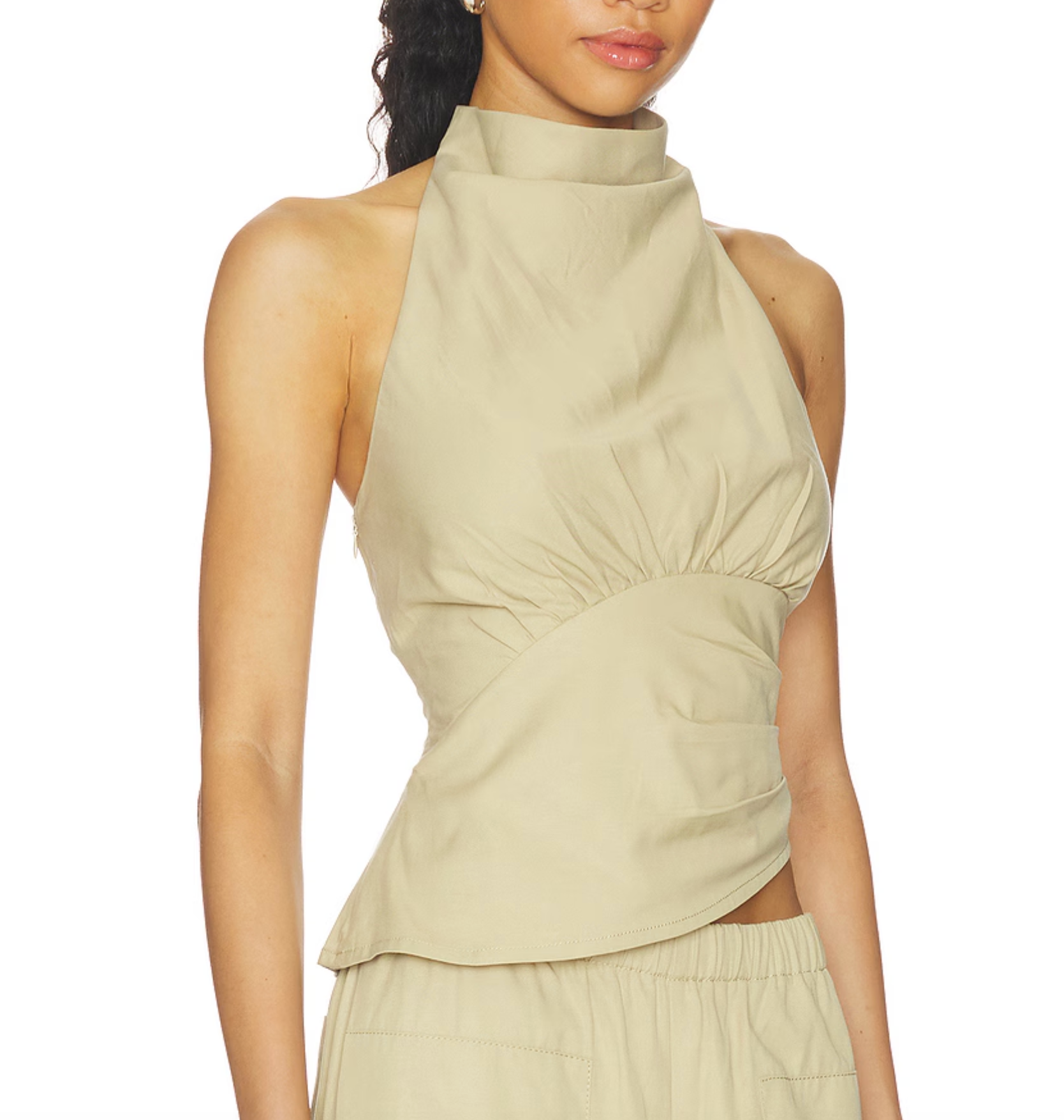A model wearing a beige halter-neck crop top with gathered draping details and a matching high-waisted skirt, shown against a plain white background.