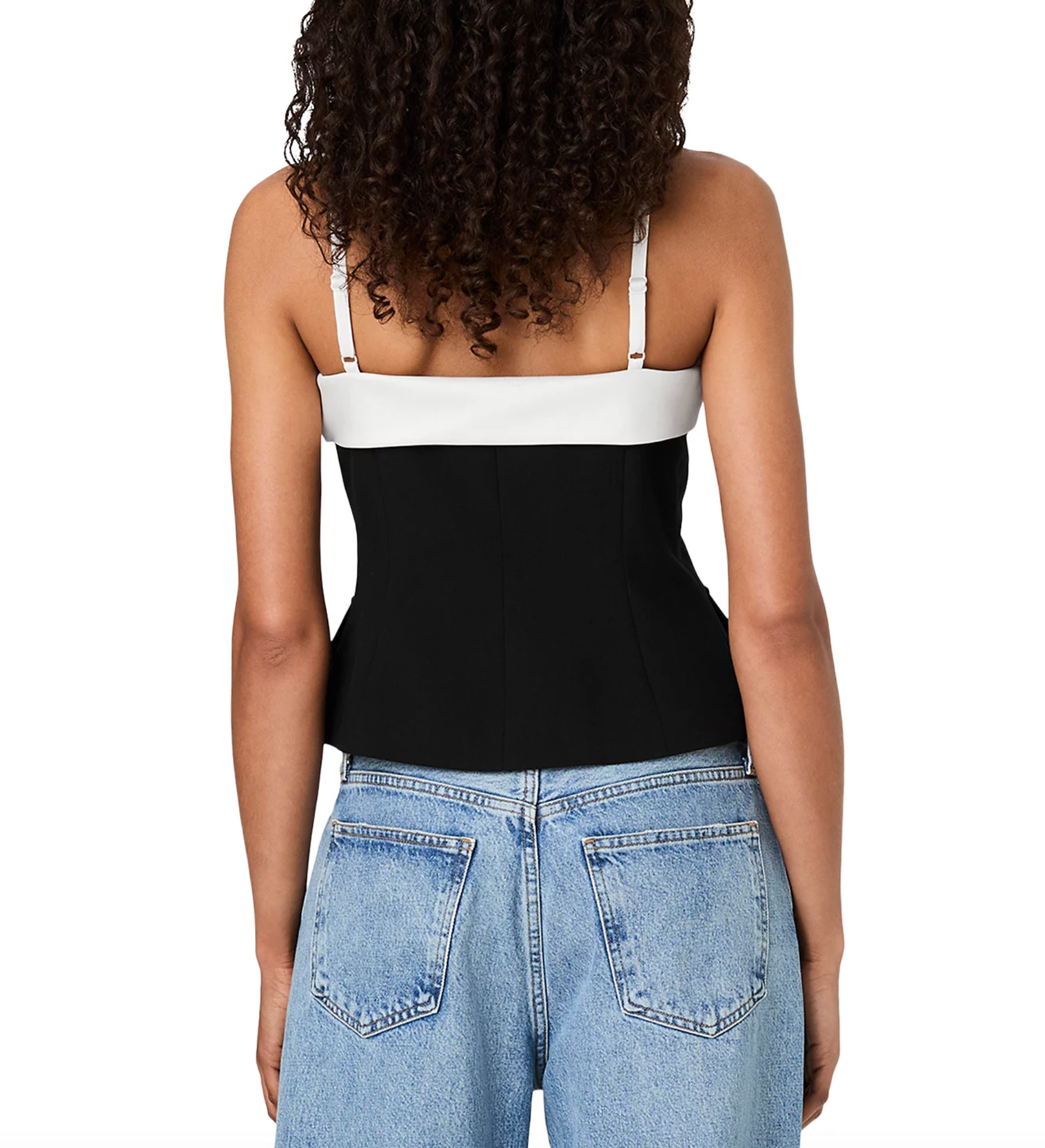 Rear view of a woman wearing a color-block camisole top with a white upper band and straps, a black lower section, and light blue jeans against a white studio background.
