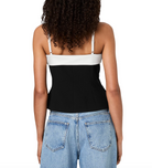Rear view of a woman wearing a color-block camisole top with a white upper band and straps, a black lower section, and light blue jeans against a white studio background.