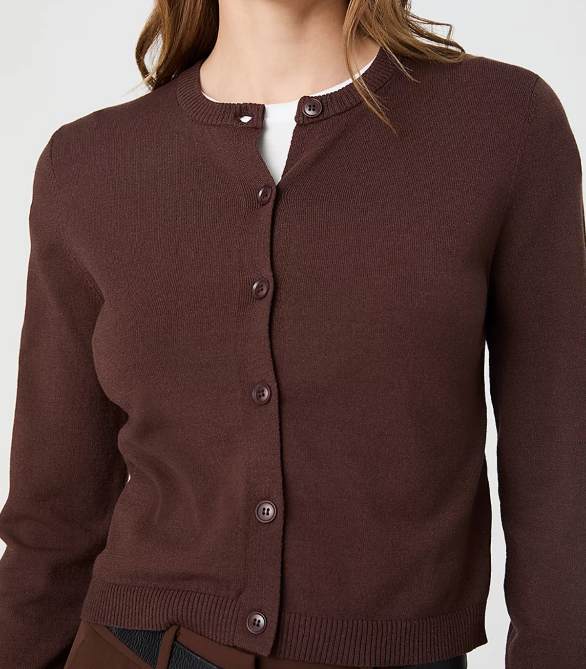 A close-up of a woman wearing a dark brown knit cardigan sweater with a button-up front, layered over a white shirt.