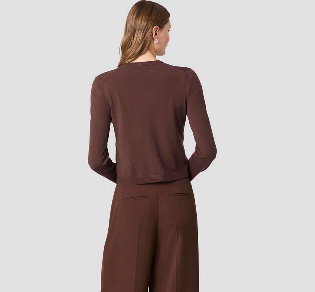 A woman shown from the back wearing a cropped, long-sleeve knit top in a dark brownish-rose shade and matching wide-leg trousers against a light gray studio background.