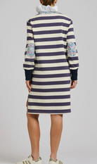 Person wearing a striped dress with floral patterns on sleeves against a plain background