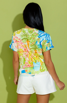Person wearing a colorful floral top and white shorts against a green background