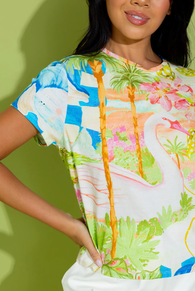 Woman wearing a colorful shirt with flamingo and palm tree design against a green background